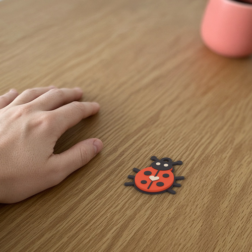 Bug Keychain: 3D printed coral ladybug keychain lying flat on a wooden desk beside a hand for scale.