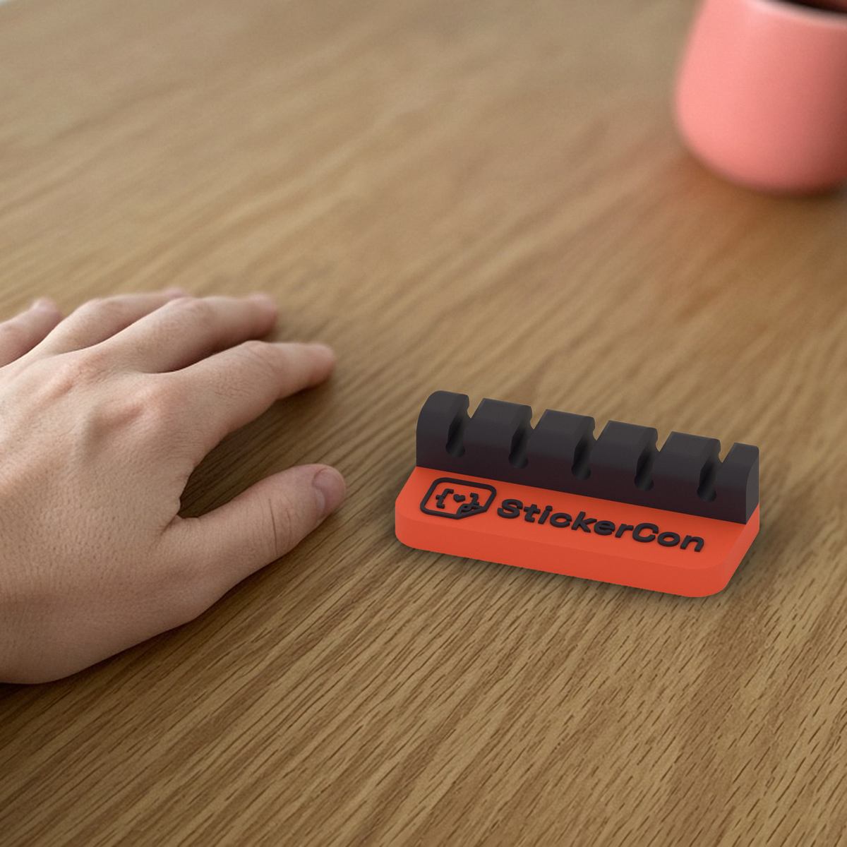 Cable Dock: 3D printed coral and black StickerCon cable dock beside a hand for scale.