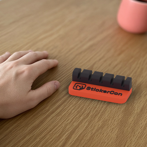 Cable Dock: 3D printed coral and black StickerCon cable dock beside a hand for scale.