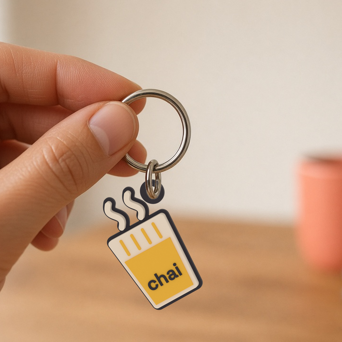 Chai Keychain: 3D printed cutting chai glass keychain with steam swirls and the word chai, hanging from a split ring held in two fingers.