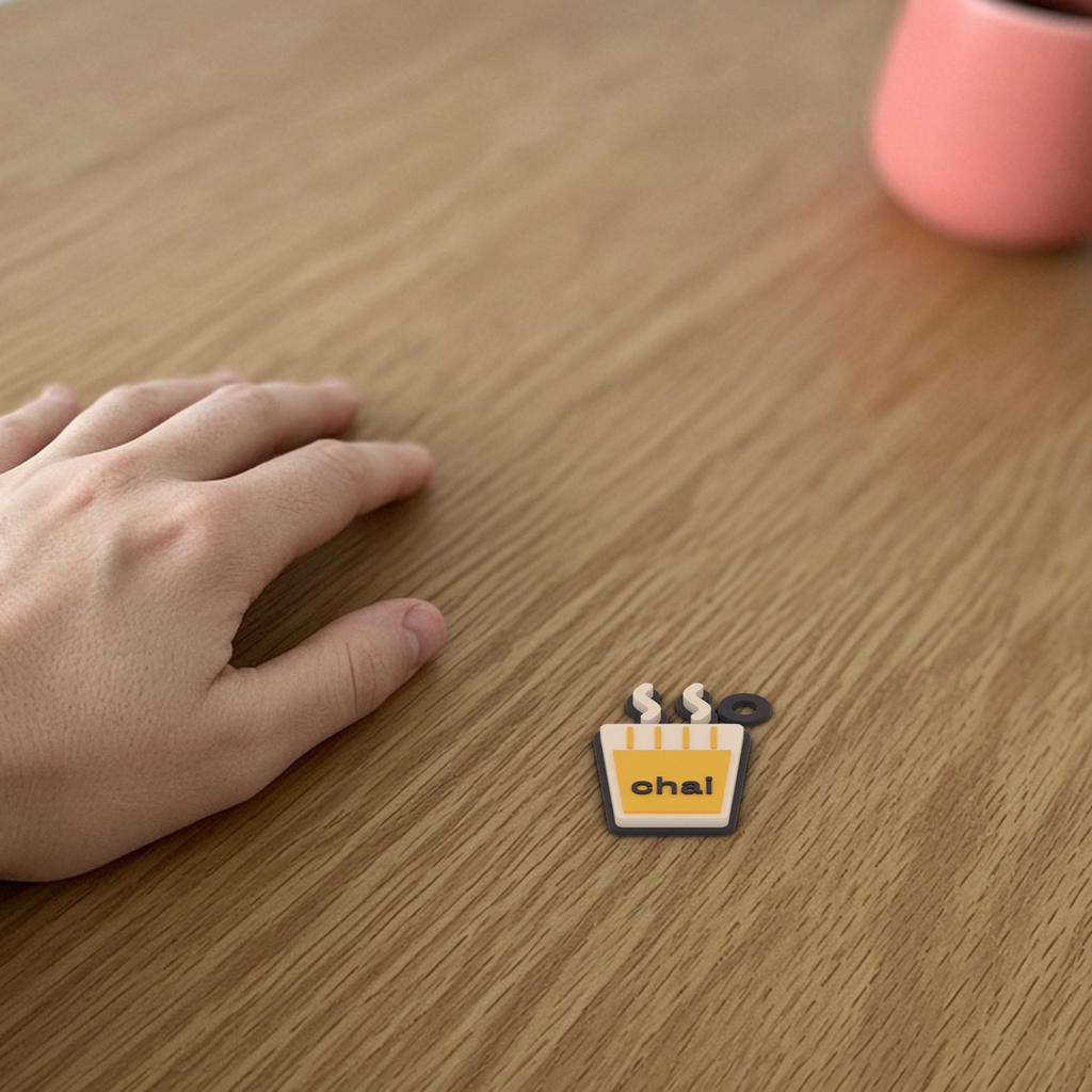 Chai Keychain: 3D printed chai glass keychain lying flat on a wooden desk beside a hand for scale.