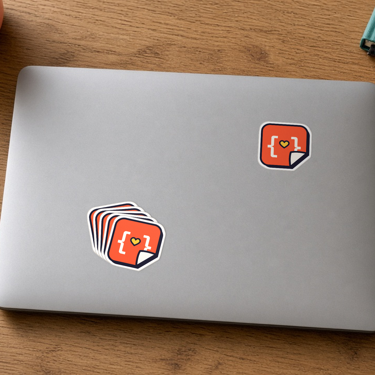 Custom Die-Cut Stickers: one StickerCon logo die-cut sticker on a silver laptop lid next to a small stack of the same sticker.