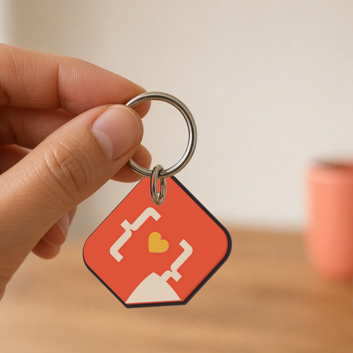 Custom Keychain: coral 3D printed StickerCon logo keychain hanging from a silver split ring held between two fingers.