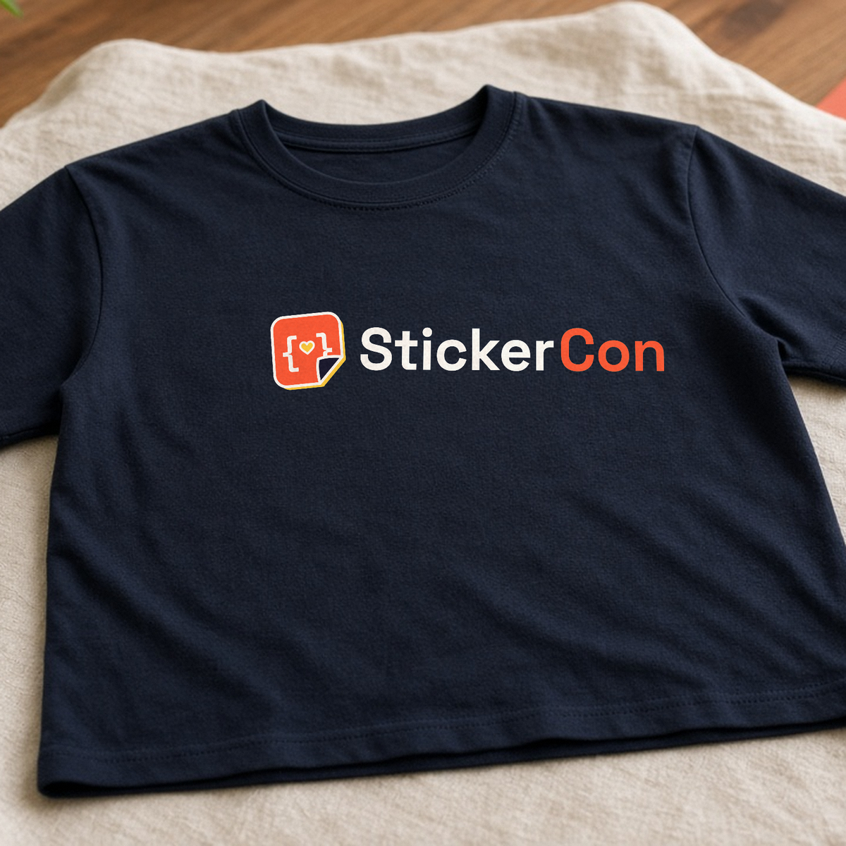 Custom Tees: navy tee with a StickerCon logo chest print, laid flat on a cream cloth.