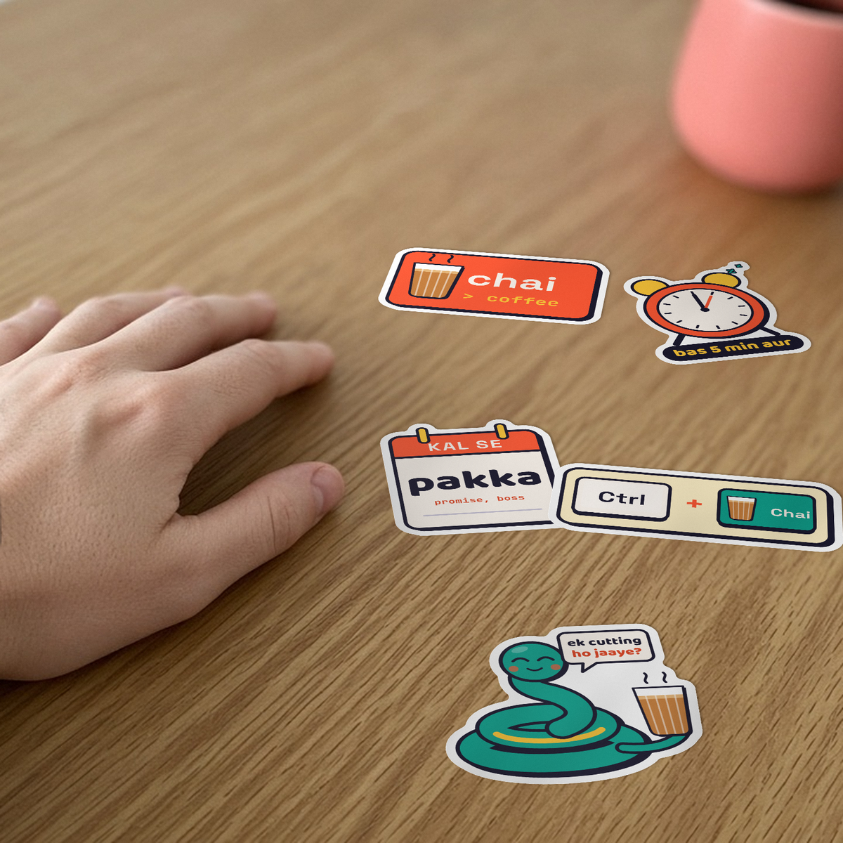 Desi Dev Sticker Pack: five stickers, including Chai > Coffee, Bas 5 min aur and Ctrl + Chai, on a desk beside a hand.
