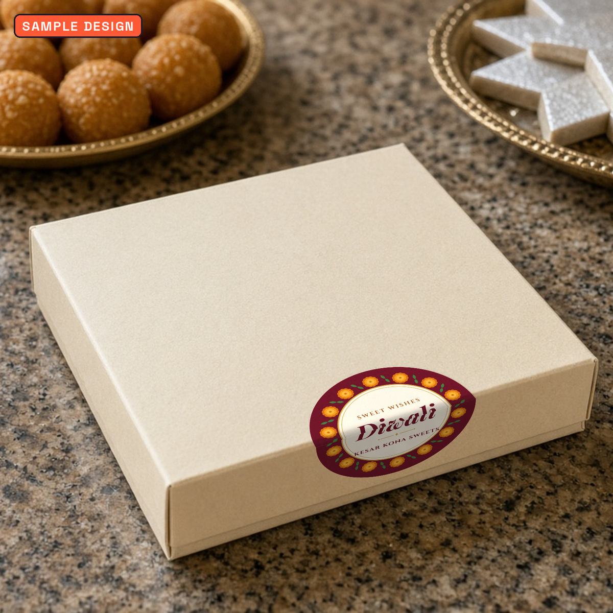 Diwali box seal sticker, 75 mm marigold design for Kesar Kona Sweets, folded over the edge of a cream sweet box with laddoos and kaju katli behind, sample design for a made-up sweet shop