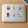 Going Home Sticker Pack: six die-cut vinyl stickers on a laptop lid, including Window Seat, Homebound suitcase, Kulhad Cat, Laddoo Siblings, 3:30 AM Club and Senior Reviewer