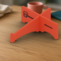 Laptop Stand: coral 3D printed cross-shaped laptop stand with the StickerCon logo, on a wooden desk.