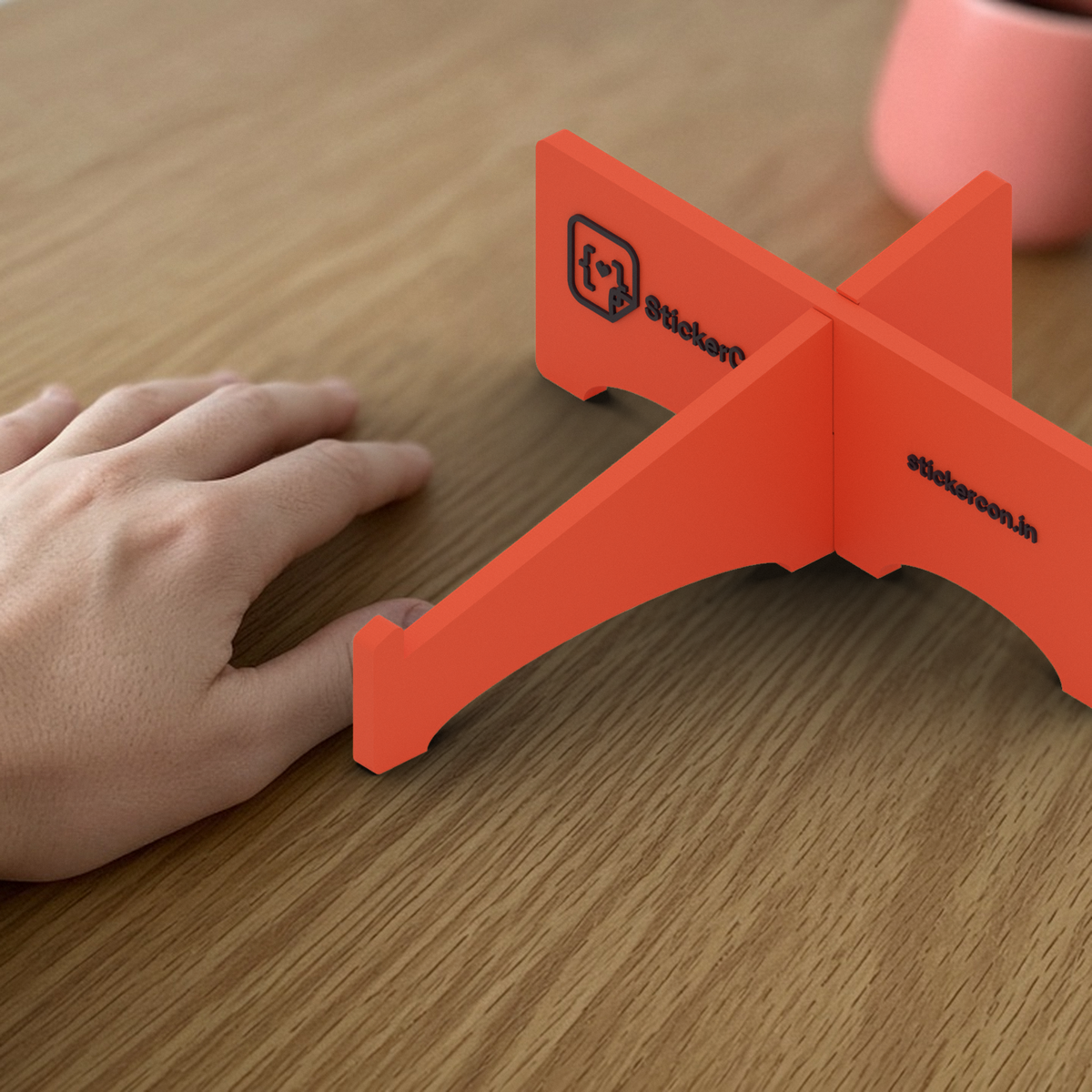 Laptop Stand: coral 3D printed cross-shaped laptop stand beside a hand for scale.