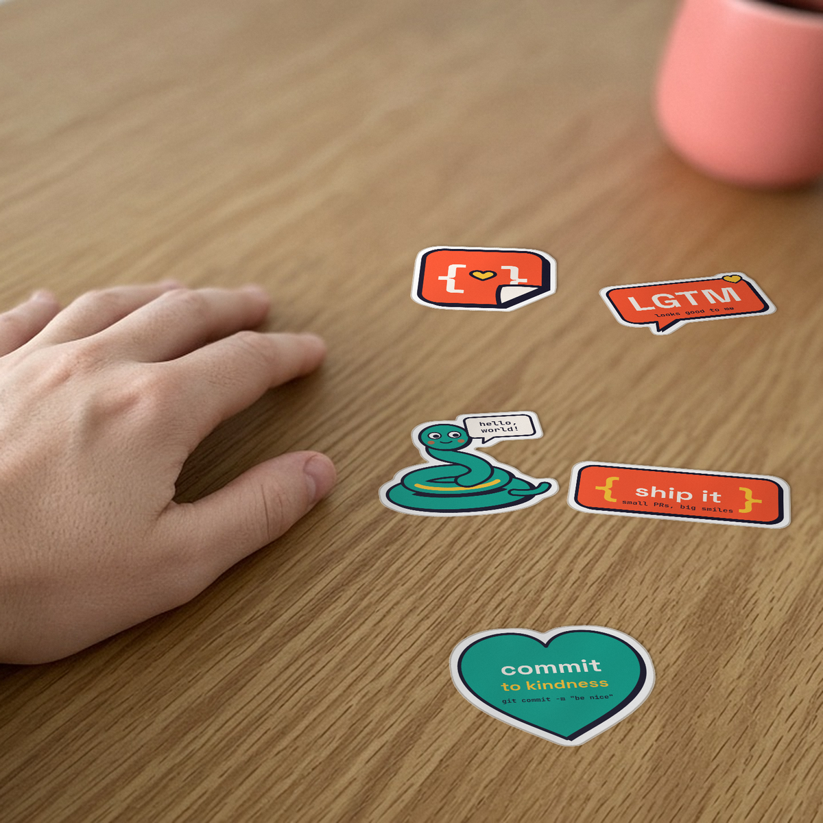 Laptop Sticker Pack: five StickerCon stickers, including LGTM, ship it and commit to kindness, on a desk beside a hand for scale.