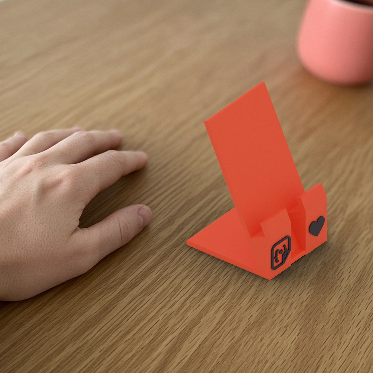 StickerCon Phone Stand: coral 3D printed phone stand beside a hand for scale.