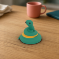 Pip the Snake Desk Mascot: 3D printed teal snake with a yellow stripe on a wooden desk with a coral mug behind.