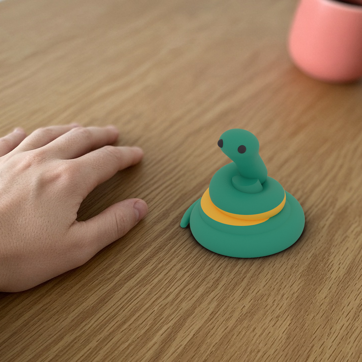 Pip the Snake Desk Mascot: 3D printed teal snake with a yellow stripe beside a hand for scale.