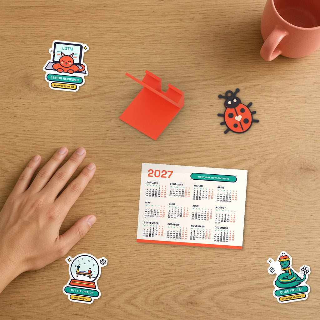 Secret Santa Desk Set: 2027 calendar, phone stand, bug keychain and Holiday Mode stickers beside a hand